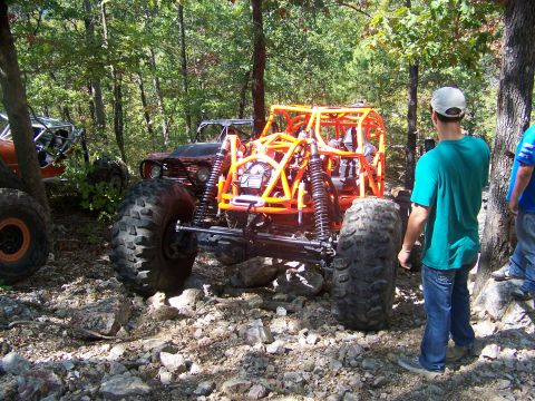 2001 Dodge 1500 - Multiple custom off-road vehicles are parked on a rocky trail surrounded by trees, with spectators observing.