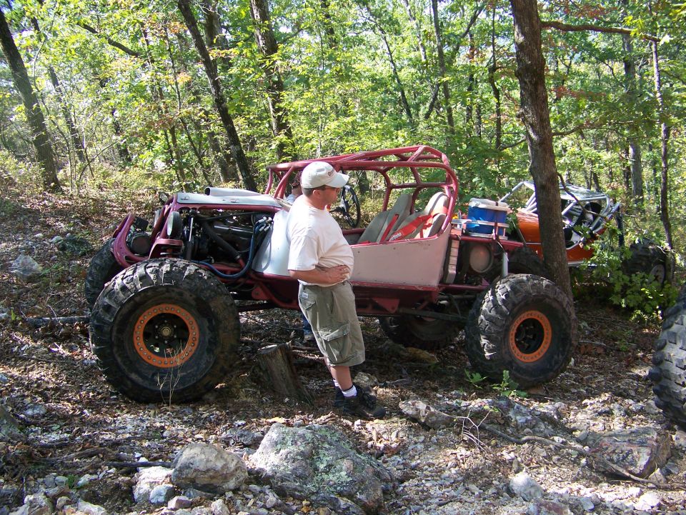 Man standing next to a custom red off-road buggy with large tires. Another buggy is visible behind it