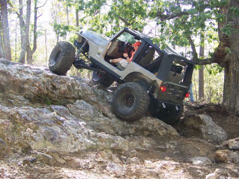 2001 Dodge 1500 - A tan Jeep Wrangler navigates a rocky incline, with its front driver's side wheel lifted high off the ground.