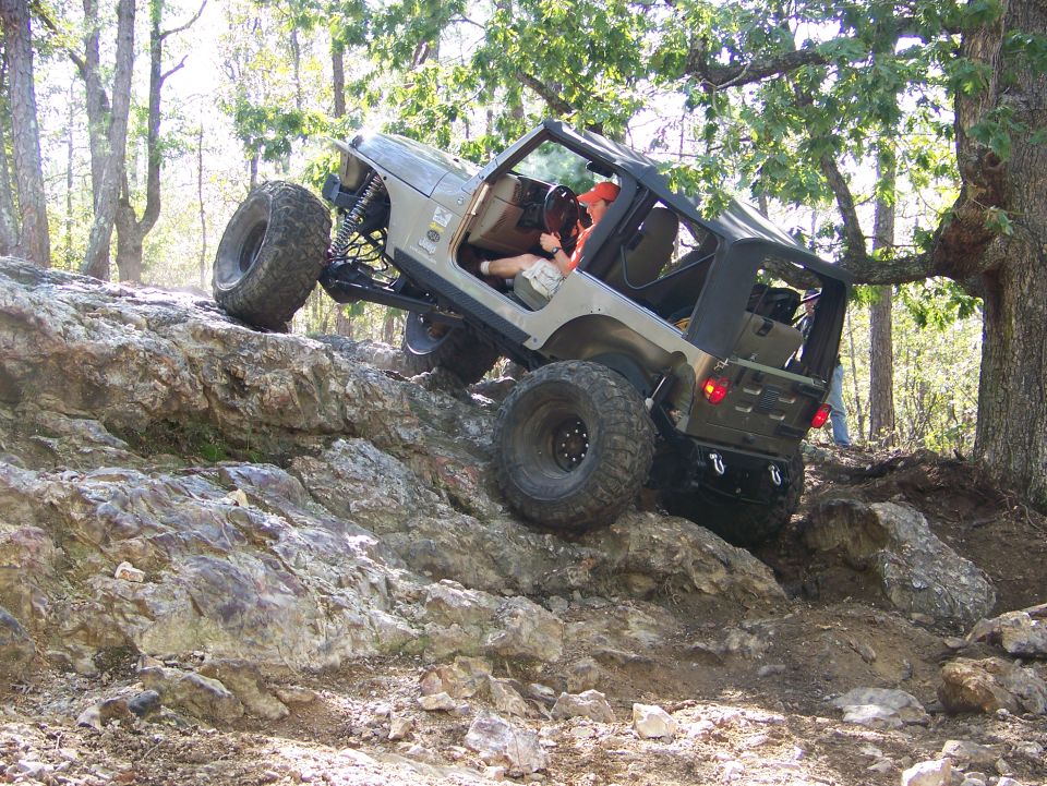 Tan Jeep Wrangler climbing rocks, front wheel high