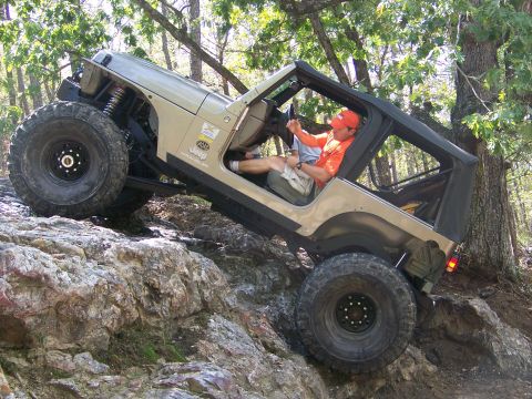 2001 Dodge 1500 - A tan Jeep Wrangler navigates a challenging rocky trail with a driver at the wheel.