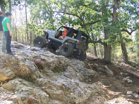 2001 Dodge 1500 - A modified Jeep Wrangler navigates a challenging rocky trail in a wooded area.