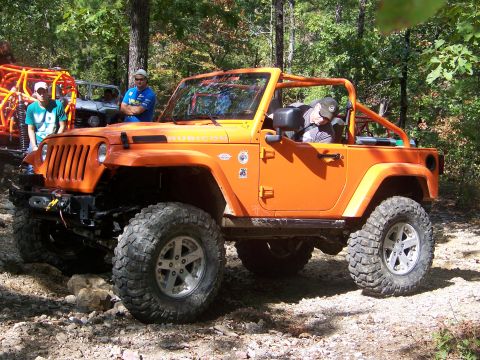 2001 Dodge 1500 - An orange Jeep Wrangler Rubicon is parked on a wooded trail with other off-road vehicles in the background.