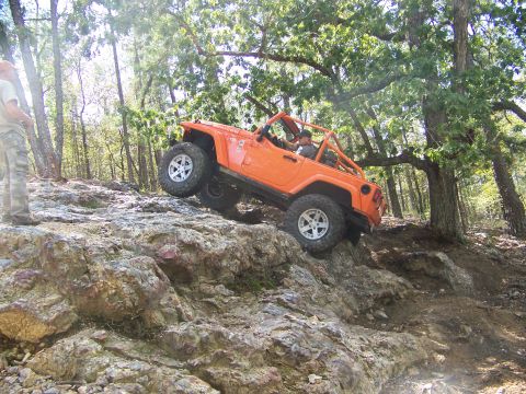 2001 Dodge 1500 - An orange Jeep Wrangler navigates a challenging rocky terrain on an off-road trail.