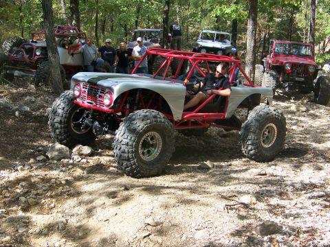 2001 Dodge 1500 - Several custom off-road vehicles are parked on a wooded trail with rocky terrain.