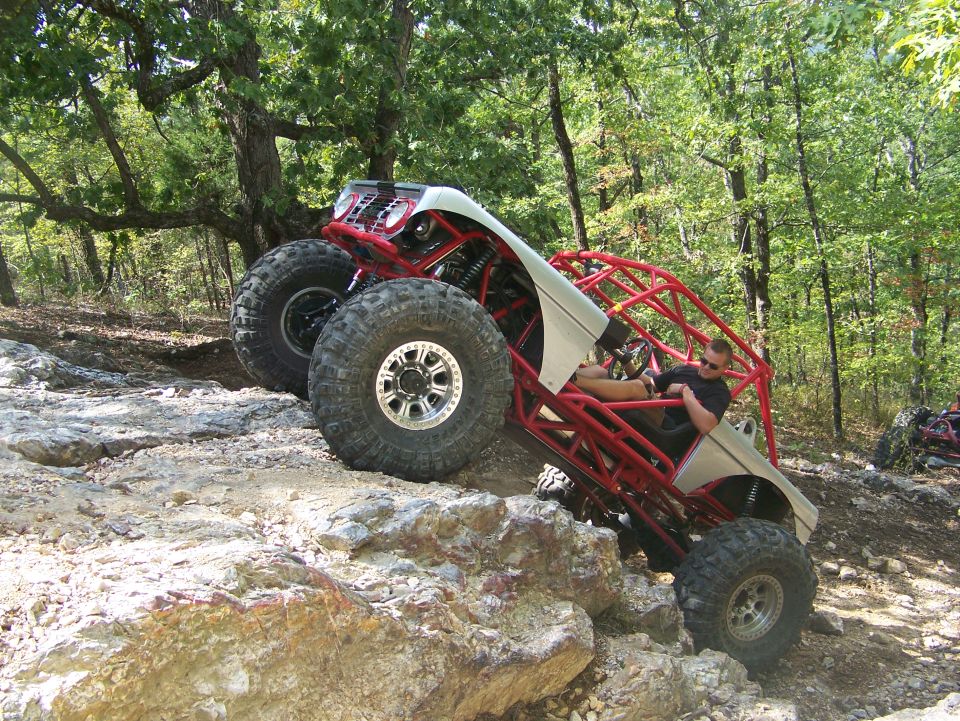Off-road buggy with red roll cage and large tires climbing rocky terrain