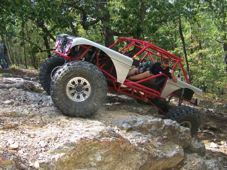 Custom buggy with red roll cage on rocky terrain. Driver is leaning on the door
