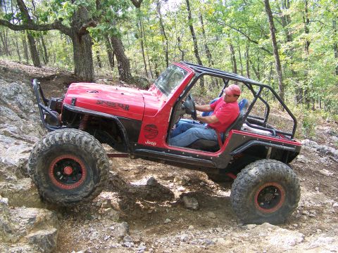 2001 Dodge 1500 - A man drives a modified red Jeep over a rocky incline in a wooded area.