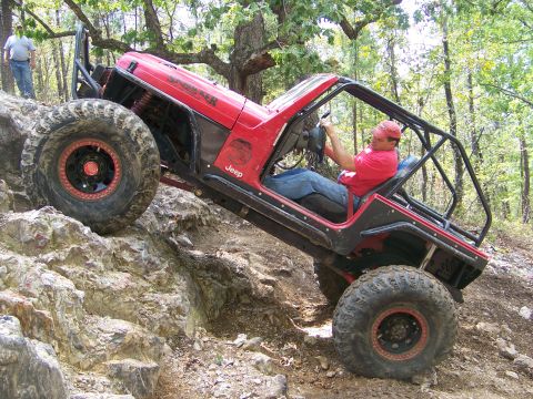 2001 Dodge 1500 - A red Jeep navigates a steep, rocky trail, its off-road capabilities with large tires and a protective roll cage.