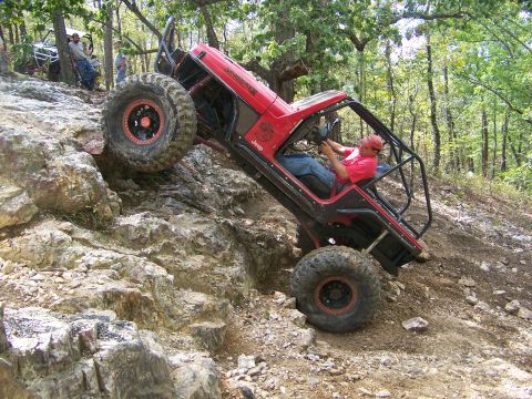 2001 Dodge 1500 - A heavily modified Jeep navigates a challenging rocky incline in a wooded area.