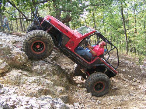 2001 Dodge 1500 - A modified red Jeep Wrangler navigates a rocky trail with a driver at the wheel.