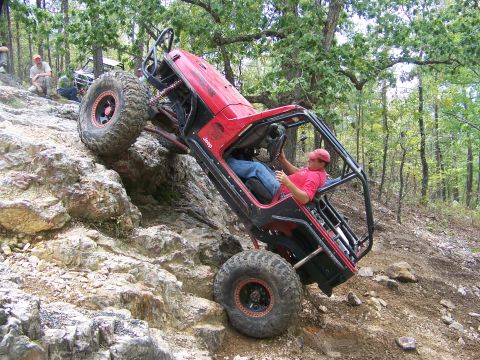 2001 Dodge 1500 - Driver navigates a red Jeep up a challenging rocky trail in a wooded area.