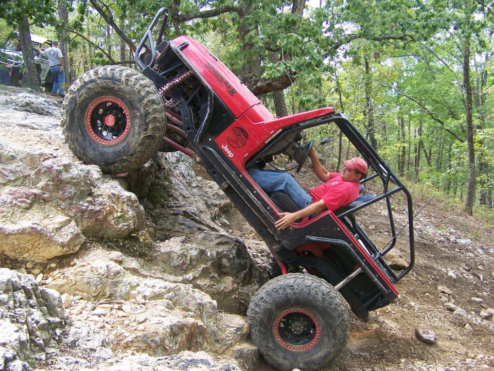 Red Jeep rock crawling on a steep incline with a person inside