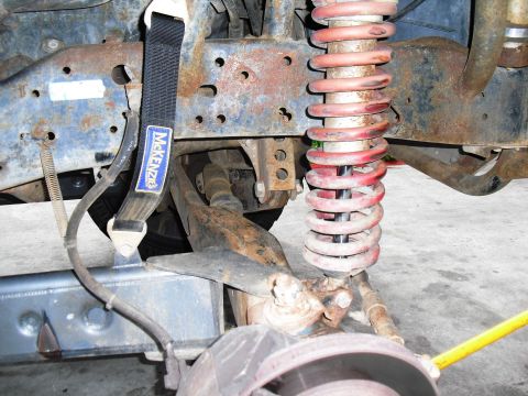 1986 Ford Bronco - Close-up view of suspension parts and a McKenzie tow strap, showing significant rust.