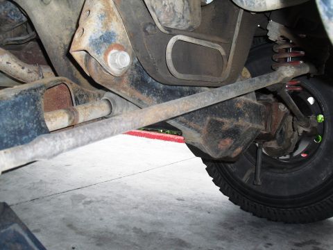 1986 Ford Bronco - Close-up of the rusty undercarriage and wheel of a vehicle, focusing on suspension components.
