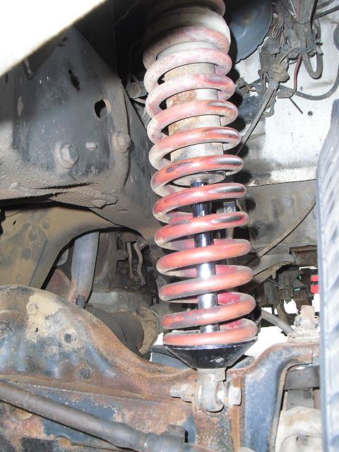 1986 Ford Bronco - Close-up view of a front suspension shock absorber and red coil spring assembly.