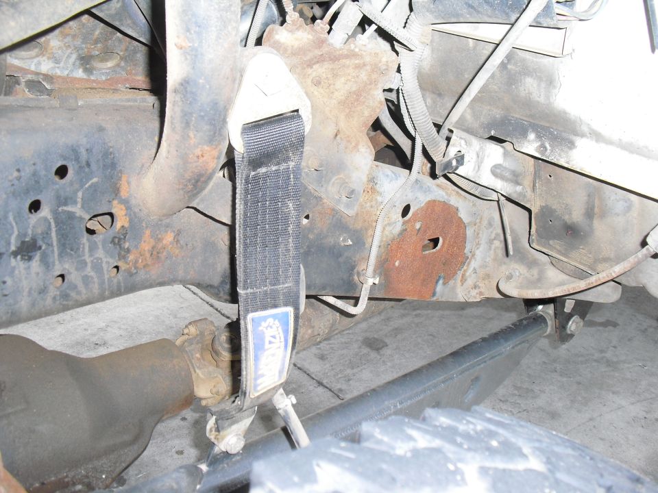 Close-up of rusty vehicle frame with a black strap and suspension parts visible