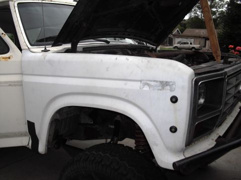 1986 Ford Bronco - White Ford Bronco with hood open, front fender and off-road tires visible. Another truck is parked in the background.