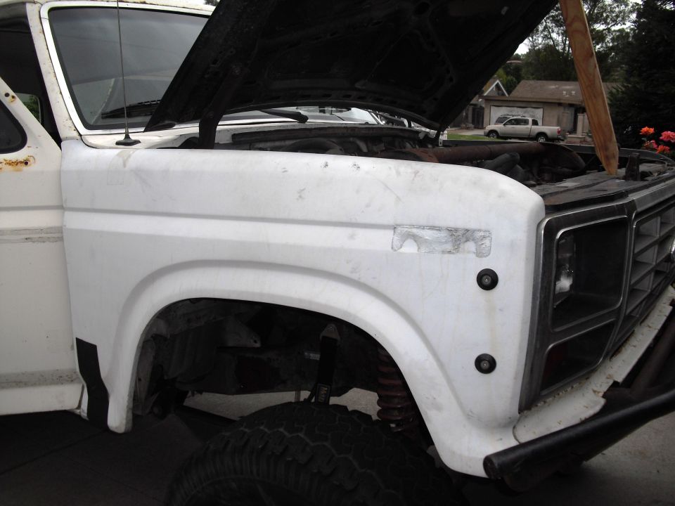 White Ford Bronco with hood open, showing engine and front fender. Off-road tires visible