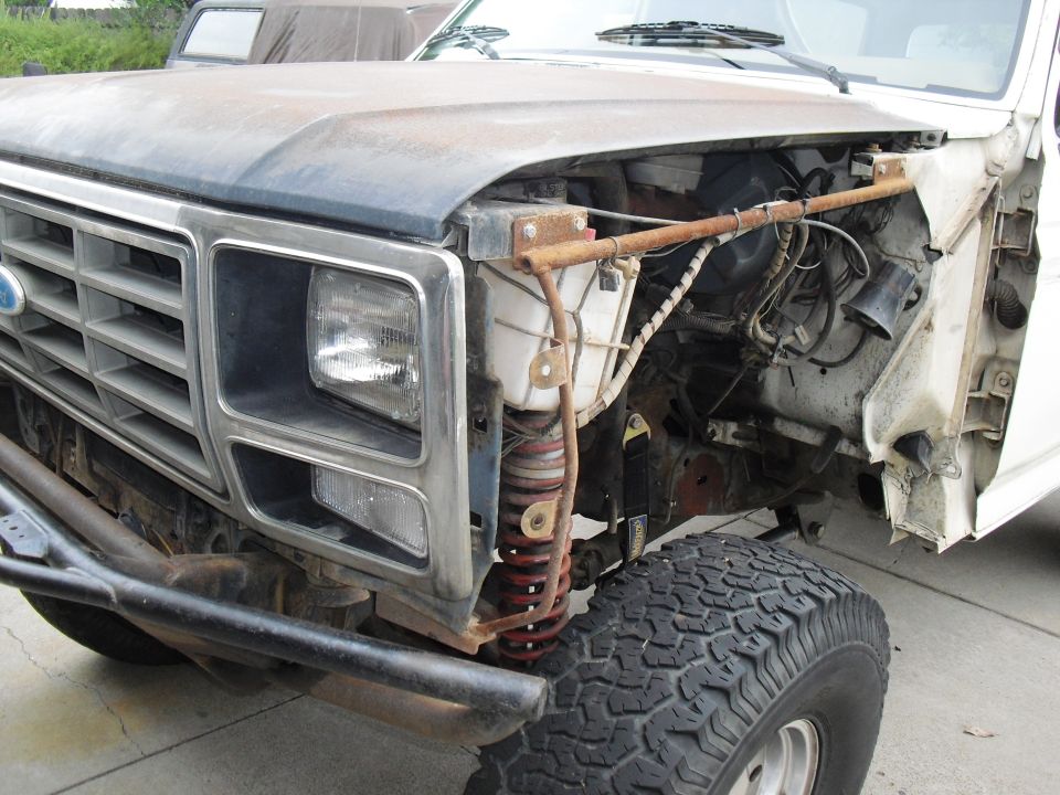 1980 Ford Bronco front end with grille, headlight, and exposed engine components. Off-road tire visible