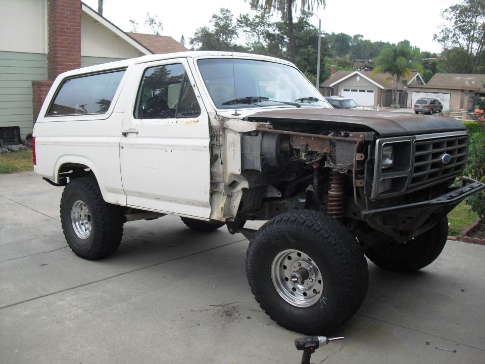 White Ford Bronco with hood removed, showing engine bay. Front fender is missing