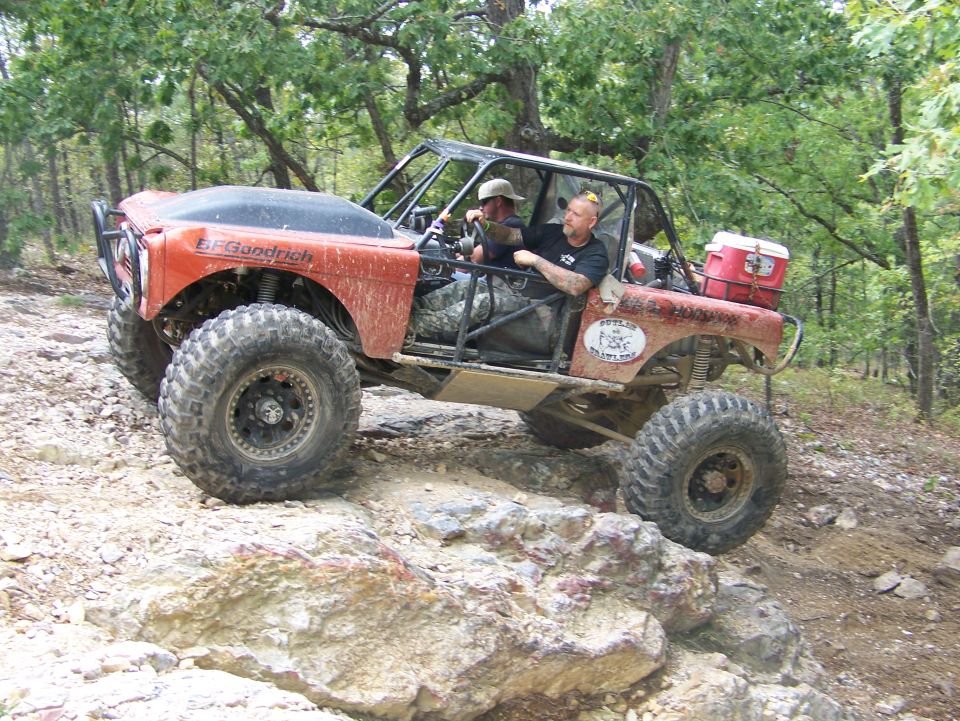 Red off-road vehicle with BFGoodrich tires on rocky terrain, two people inside
