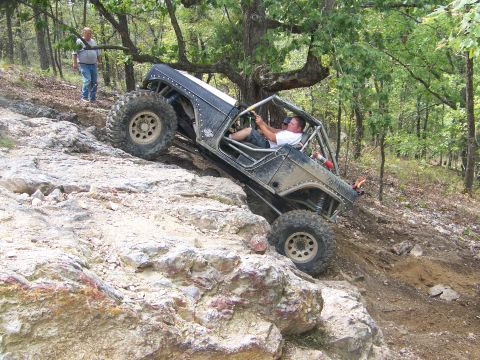 2001 Dodge 1500 - A heavily modified off-road buggy navigates a steep, rocky incline in a wooded area.