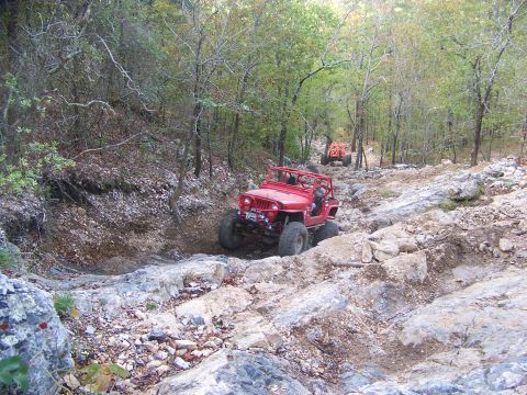2001 Dodge 1500 - Two off-road vehicles navigate a challenging, rocky path through a wooded area.