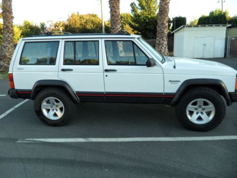 1994 Jeep Cherokee - A white Jeep Cherokee is seen from the side, parked in a lot with palm trees in the background.