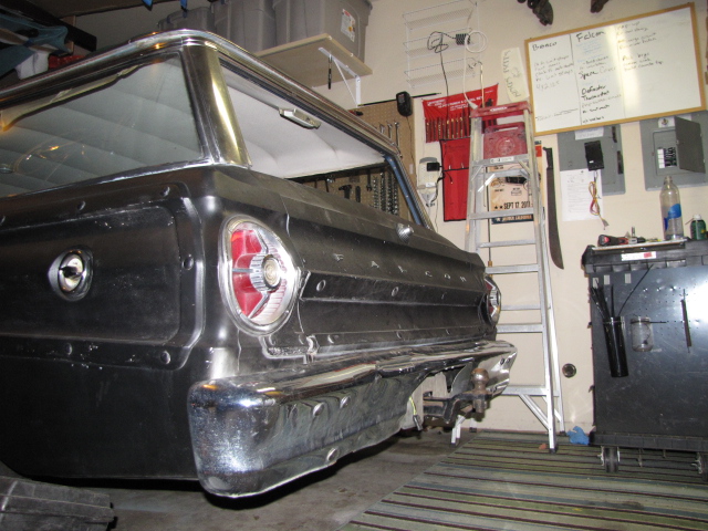 1965 Ford Falcon wagon rear view, showing taillight, bumper, and trailer hitch. Garage interior with tools an…
