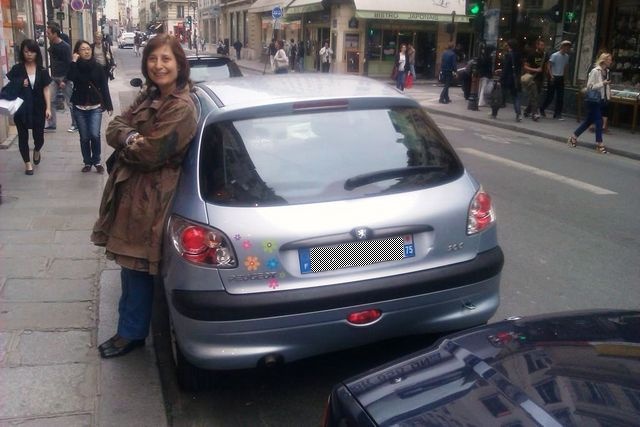 Silver Peugeot 206 hatchback parked on a city street, rear view. A woman leans against it