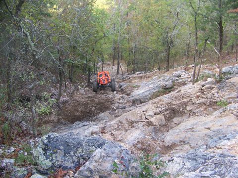 2001 Dodge 1500 - An orange off-road vehicle navigates a challenging rocky terrain in a wooded area.