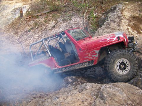 2001 Dodge 1500 - A red Jeep Wrangler, modified for off-roading, maneuvers through a challenging rocky landscape, kicking up dust and smoke.