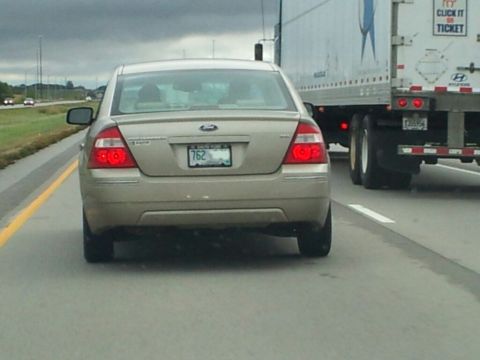 2003 Ford Crown Victoria - A gold sedan is seen from behind on a highway, next to a large truck.