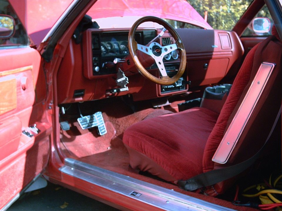 Red El Camino interior with wood-rim steering wheel and cloth bucket seat