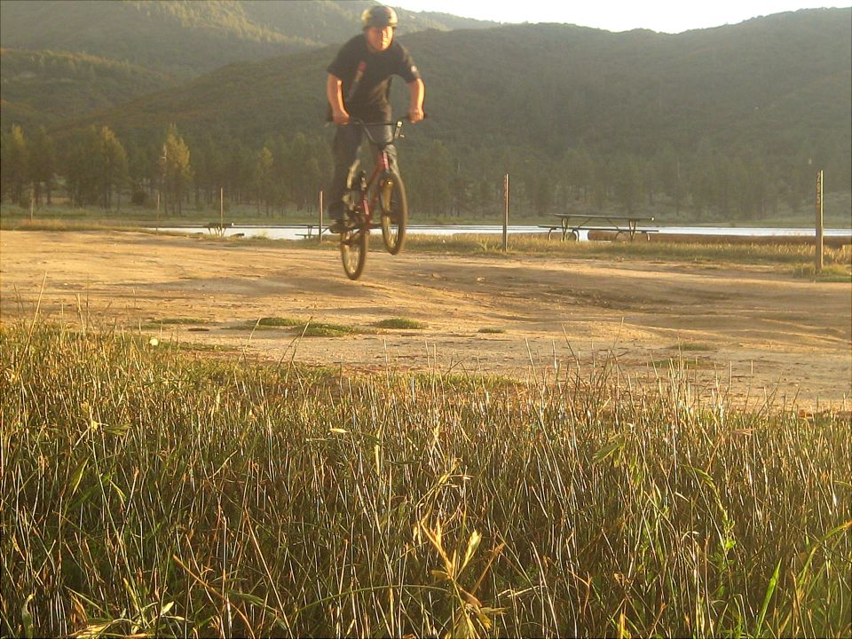 Person on a bicycle mid-air over a dirt path with a lake and hills in the background