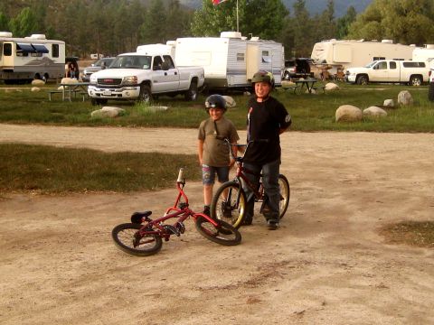1996 Ford Bronco - Two boys with bicycles at a campsite, with RVs and trucks visible in the background.