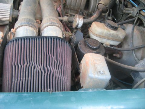 1990 Ford Bronco - Close-up view of an engine bay, showing various components and hoses. The green fender is partially visible.