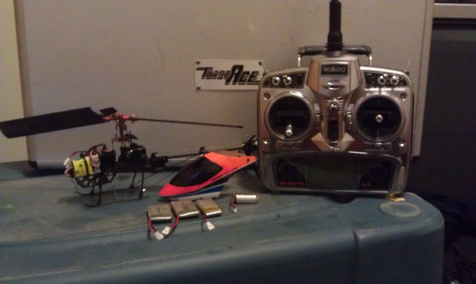 Two remote control helicopters and a transmitter with batteries on a blue surface