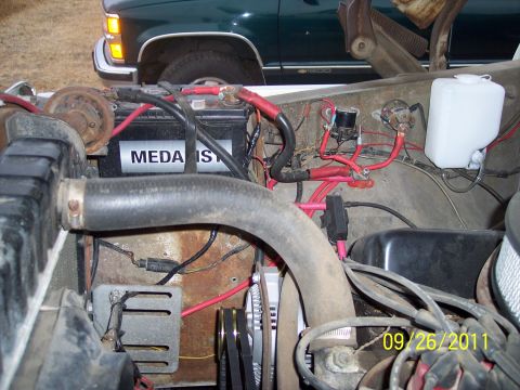 1973 Ford F-250 - The engine bay of a vehicle shows the battery, hoses, and alternator, with another vehicle in the background.