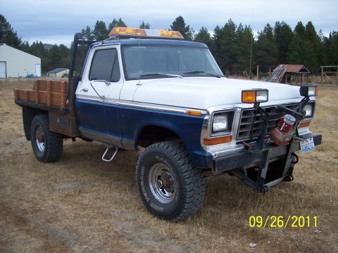 1973 Ford F-250 - A two-tone white-over-blue Ford pickup with a flatbed body and wooden side rails, viewed from the front three-quarter angle, parked in a dr…