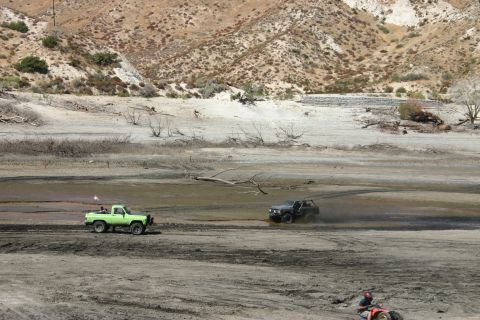 1991 Ford Bronco - Two off-road vehicles navigate a muddy, dry terrain under a bright sky.