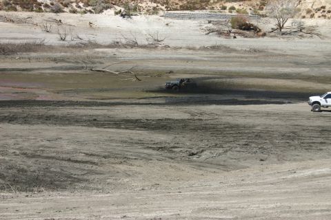 1991 Ford Bronco - Two off-road vehicles are visible in a dry lake bed with sparse vegetation and hills in the background.