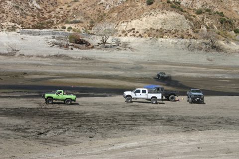1991 Ford Bronco - Several trucks are seen driving in a dry, dusty landscape, with a green pickup truck in the foreground.