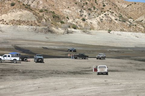 1991 Ford Bronco - Multiple trucks and SUVs gathered in a dry lake bed with hills in the distance.