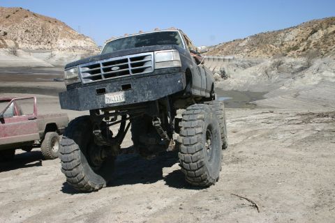 1991 Ford Bronco - A heavily modified black Ford F-Series truck with oversized tires sits in a dry, dusty landscape.