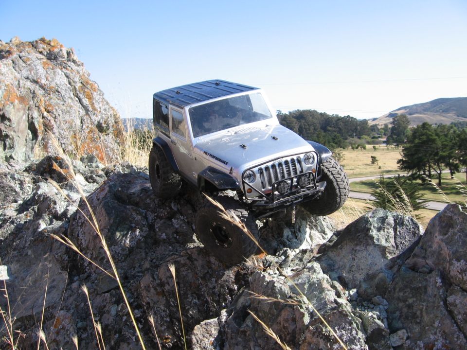 RC rock crawler Jeep Wrangler climbing over rocks on a sunny day
