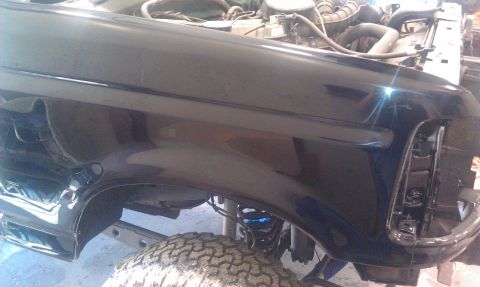 1995 Ford Bronco - Front fender and engine bay of a black Ford Bronco, showing its mechanical components and tire.