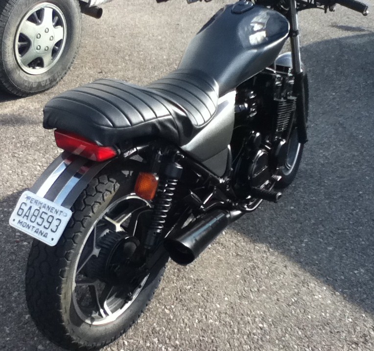 Black motorcycle parked on asphalt, showing rear wheel, seat, and license plate