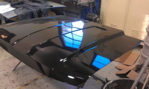 1995 Ford Bronco - A freshly painted black car hood rests on a stand in a workshop environment.